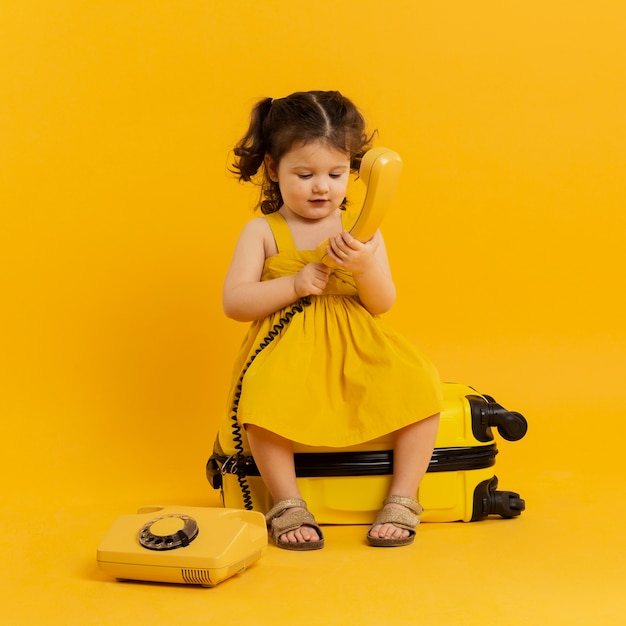 Free photo front view of adorable child posing with telephone and luggage
