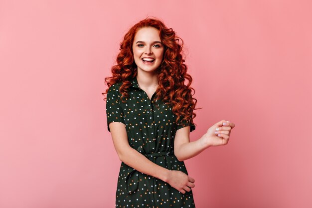 Front view of adorable ginger girl isolated on pink background. Studio shot of smiling curly young woman looking at camera.