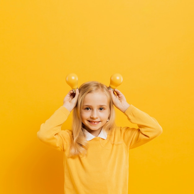 Free photo front view of adorable girl posing while holding yellow light bulbs