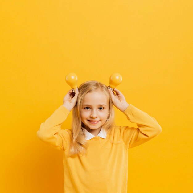 Front view of adorable girl posing while holding yellow light bulbs