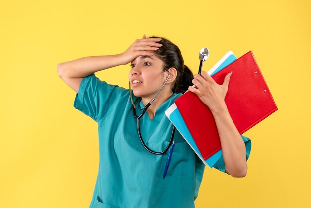 Front view agitated female doctor with documents holding her head on yellow background