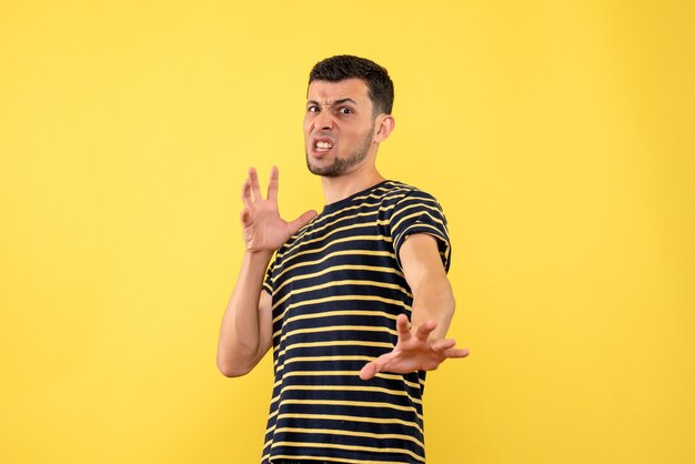 Front view agitated young male in black and white striped t-shirt yellow isolated background