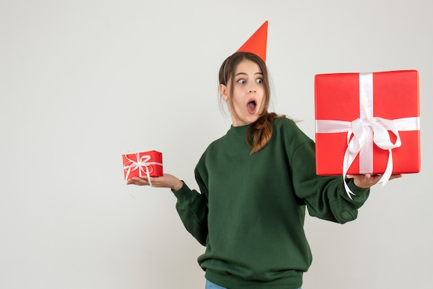Вид спереди изумленная девушка в кепке, глядя на свой большой рождественский подарок