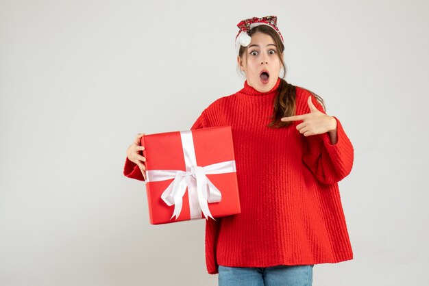 Front view amazed girl with santa hat finger pointing the gift