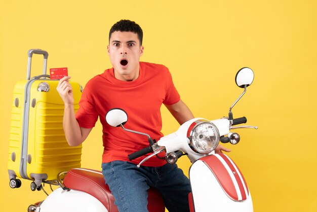 Front view amazed young man on moped holding credit card