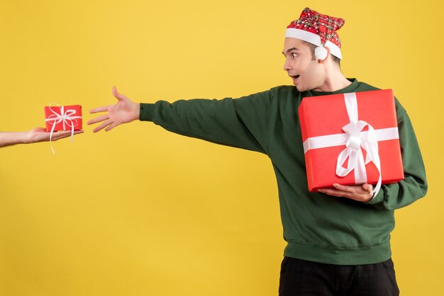 Front view amazed young man trying to catch the gift in female hand standing on yellow 