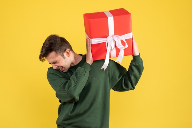 Vista frontale stupito giovane uomo con maglione verde azienda regalo su giallo