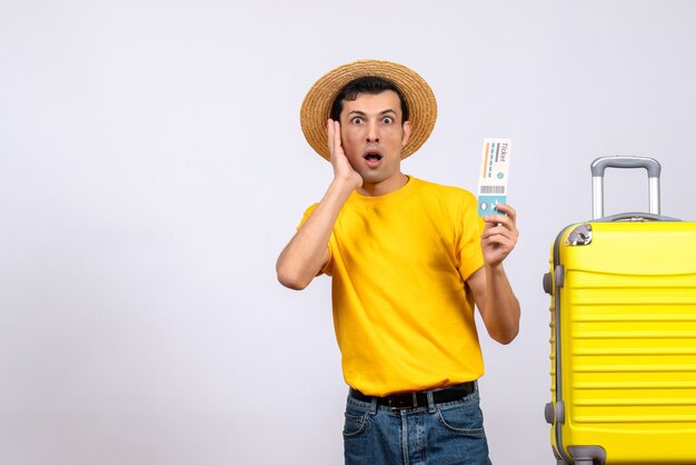 Front view amazed young tourist in yellow t-shirt standing near yellow suitcase