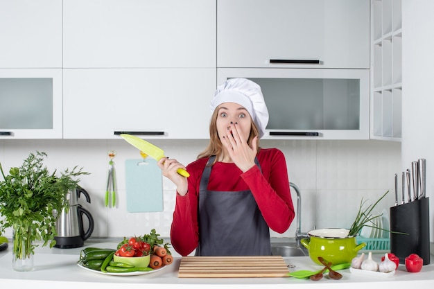 Foto gratuita vista frontale stupita giovane donna in grembiule che regge coltello