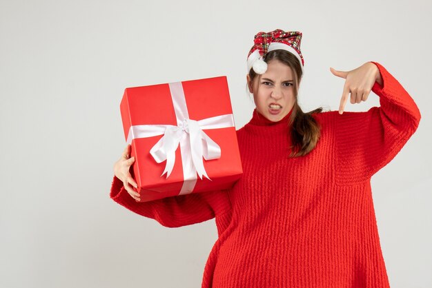 Front view angry girl with santa hat holding present finger pointing down standing