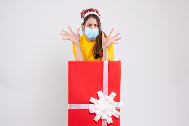 Front view angry girl with santa hat opening her hands standing behind big xmas gift