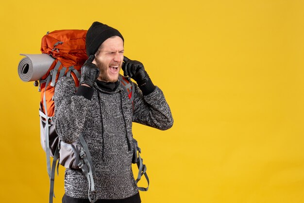 Front view of angry male hitchhiker with leather gloves and backpack closing ears with fingers