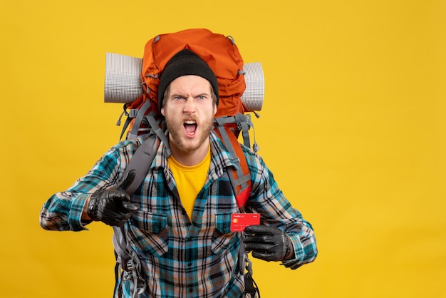 Front view of angry man with backpacker holding credit card pointing at front