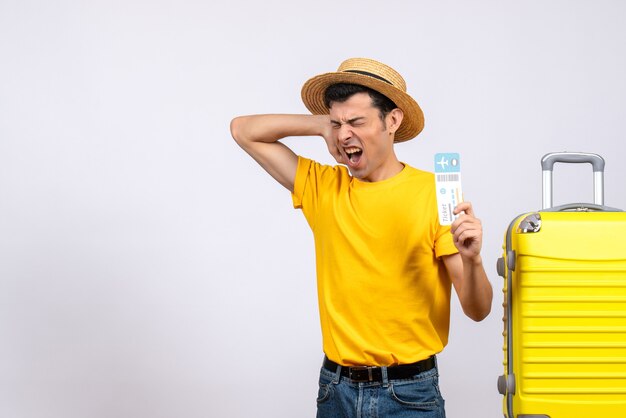 Front view angry tourist in yellow t-shirt standing near yellow suitcase holding ticket