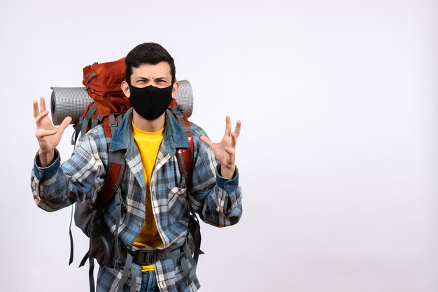 Front view angry young hiker with backpack and mask raising hands