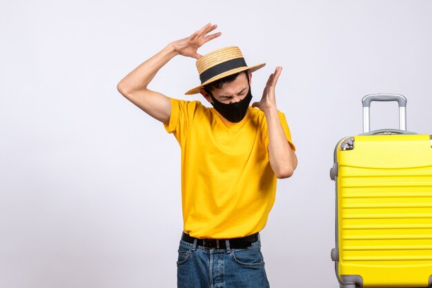 Front view angry young man in yellow t-shirt standing near yellow suitcase