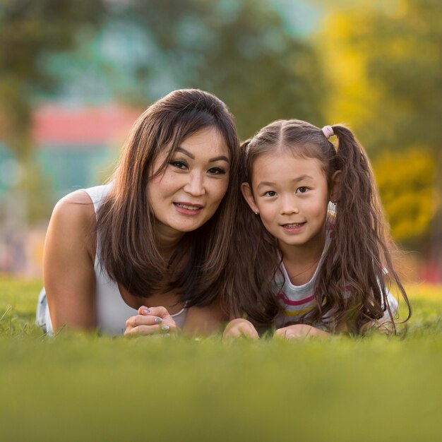 Front view asian mother and daughter staying on grass