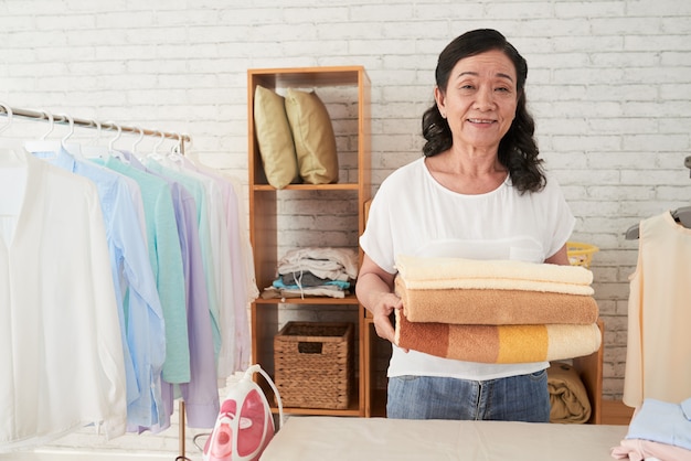 Front view of Asianhousemaid standing with towels in laundry room