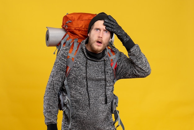 Front view of astonished male hitchhiker with leather gloves and red backpack