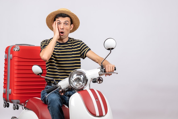 Front view of astonished young man with straw hat on moped looking at camera