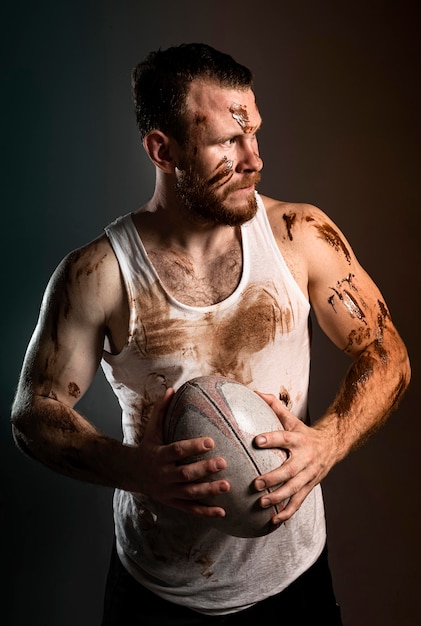 Вид спереди спортивного грязного игрока в регби, держащего мяч