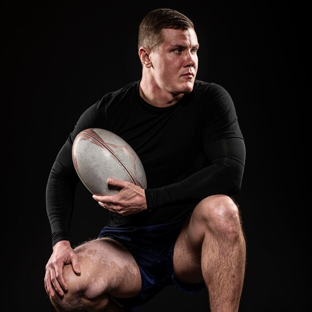 Front view of athletic handsome rugby player holding ball while posing
