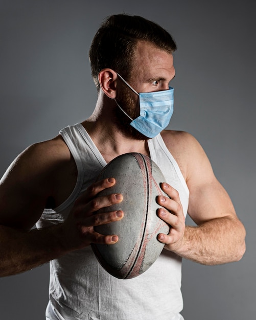 医療マスクを着用しながらボールを保持しているアスリート男性ラグビー選手の正面図