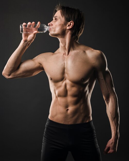 Front view of athletic shirtless man drinking water from bottle