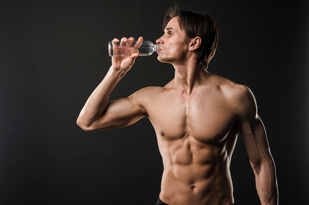 Front view of athletic shirtless man drinking water