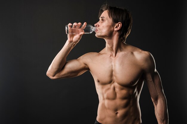 Front view of athletic shirtless man drinking water
