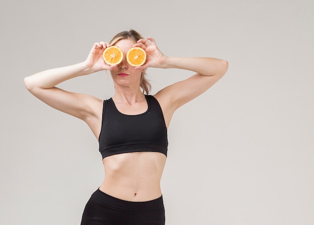 Вид спереди спортивная женщина держит оранжевые половинки над ее глазами
