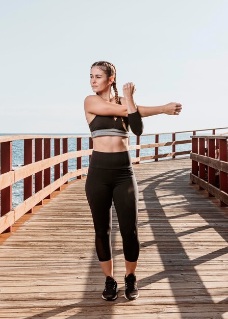 Front view of athletic woman stretching outdoors by the beach