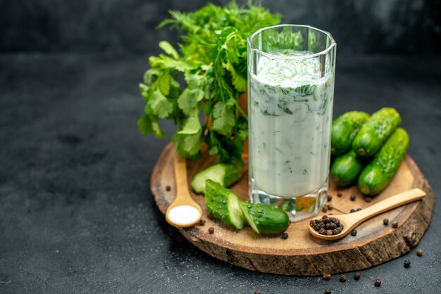 Front view atlama in glass chopped cucumber black pepper and salt in spoon on wood board on dark isolated table