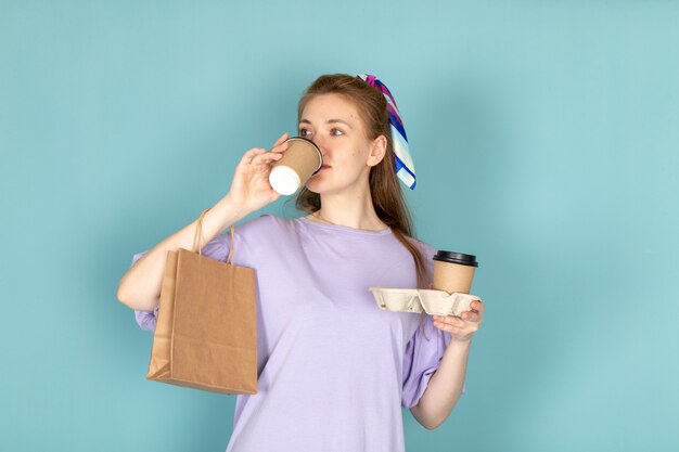 Вид спереди привлекательная женщина в синем платье-рубашке, держащая бумажный пакет и кофейные чашки, пьющие на синем