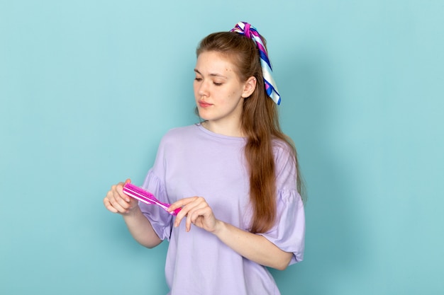 A front view attractive female in blue shirt-dress holding pink brush on blue