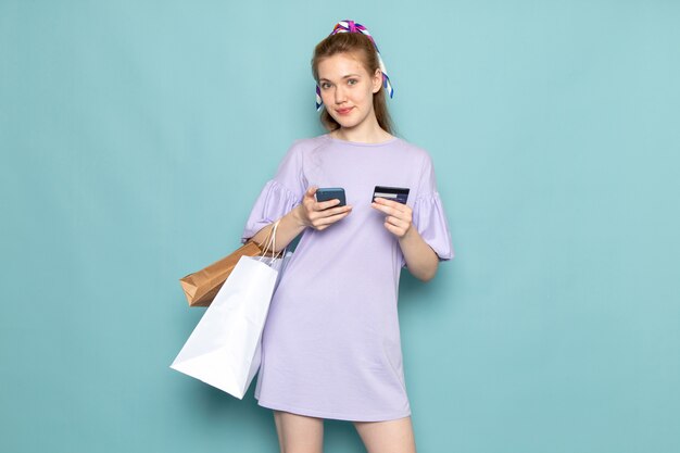 A front view attractive female in blue shirt-dress holding and using a phone smiling on blue