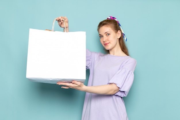 A front view attractive female in blue shirt-dress holding white shopping package on blue