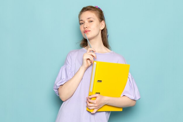 A front view attractive female in blue shirt-dress holding yellow files on blue