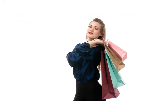 A front view attractive young lady in blue blouse black trousers posing holding shopping packages on the white background fashion elegant clothing