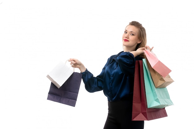 A front view attractive young lady in blue blouse black trousers posing holding shopping packages on the white background fashion elegant clothing