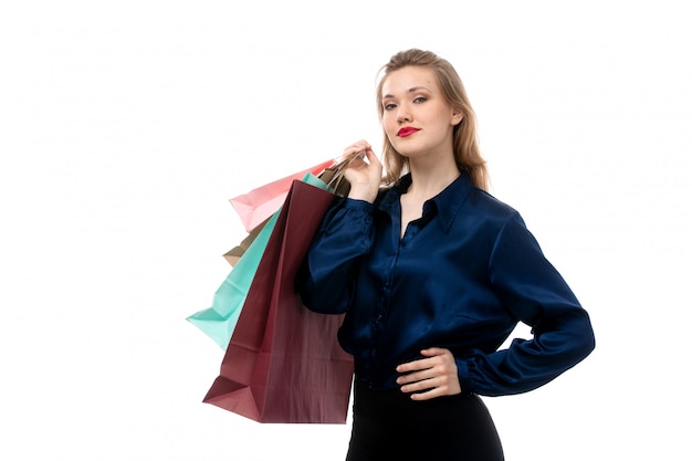 A front view attractive young lady in blue blouse black trousers posing holding shopping packages on the white background fashion elegant clothing