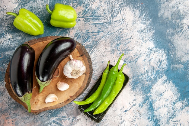 Free photo front view aubergines garlic on tree wood board peppers hot green peppers on black plate on blue-white background free space