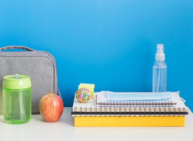 Vista frontale di nuovo ai materiali scolastici con taccuino e disinfettante per le mani