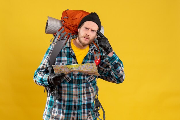 Front view of baffled young tourist with leather gloves and backpack holding map