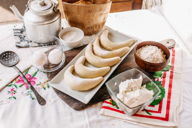 Вид спереди рогалики внутри белой тарелки вкуснятина сладкая вместе с мукой и яйцами на столе продукты печенья