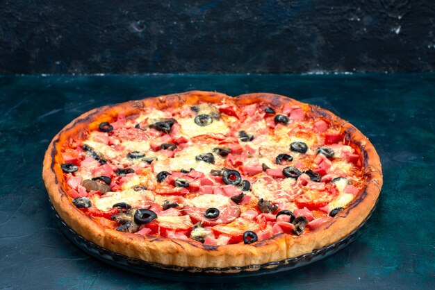 Вид спереди испеченная вкусная пицца с оливками, сосисками и сыром на синем столе.