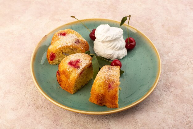 A front view baked fruit cake delicious sliced with red cherries inside and sugar powder inside round green plate on pink