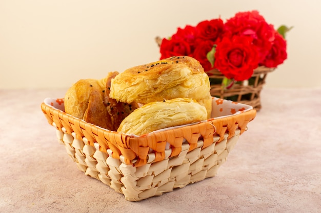 Una vista frontale ha cotto i panini al forno orientali di qogals freschi caldi dentro lo scomparto del pane con i fiori rossi sulla tavola e sul colore rosa