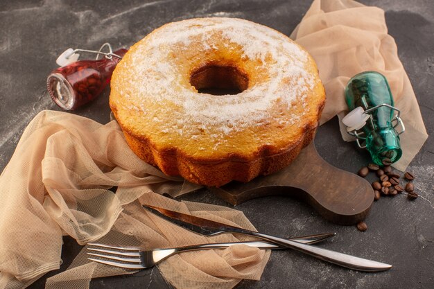 A front view baked round cake with sugar powder and coffee seeds on the wooden desk