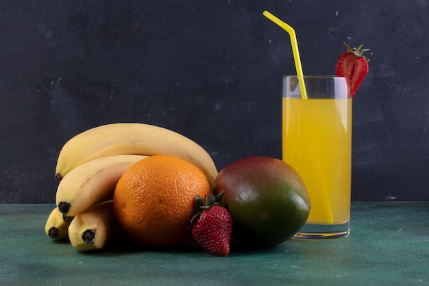 Foto gratuita banane vista frontale con fragole di mango e un bicchiere di succo d'arancia